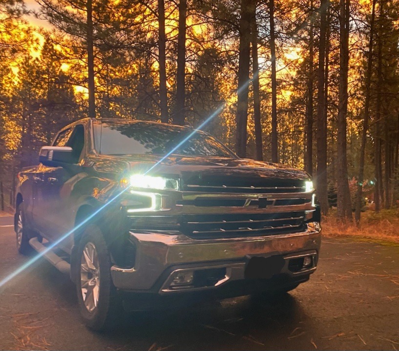 A black Chevrolet truck parked on a forest road, illuminated by sunset. Tall trees surround the vehicle, creating a vibrant, warm atmosphere.