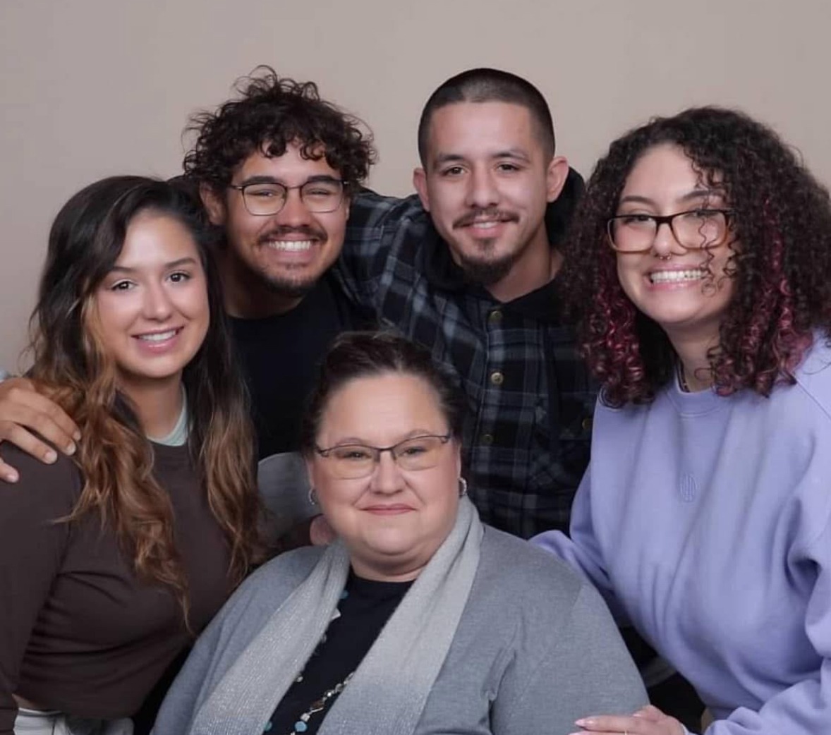 Five smiling individuals pose together, showcasing a mix of hairstyles and casual attire. The group conveys warmth and connection, likely celebrating a family moment.