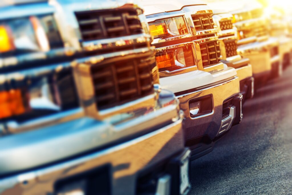 A row of shiny pickup trucks showcases their chrome grilles and headlights, emphasizing the appeal of these vehicles in a sunny setting.